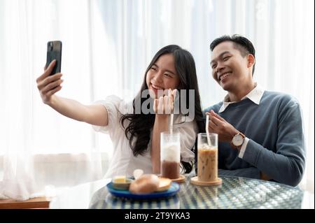 Young Asian couple having a date in a cute cafe, having good time together and playing with smartphone. Couple concept. Stock Photo