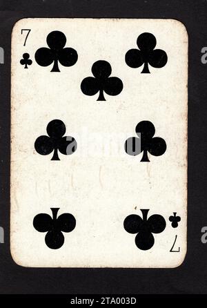 A vintage seven of clubs playing card isolated on a black background. Stock Photo