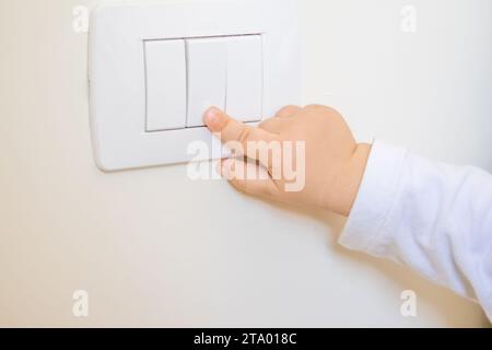 adorable little boy child turning on the white light-switch with his finger of little hand Stock Photo