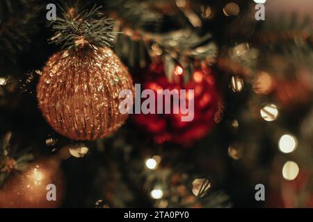 Detailed golden red glossy Christmas ball hanging on a Christmas tree with magic garland lights. Decorated spruce branches. Stock Photo