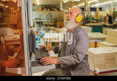 Man using computer on a cutting machine in a woodworking workshop Stock Photo