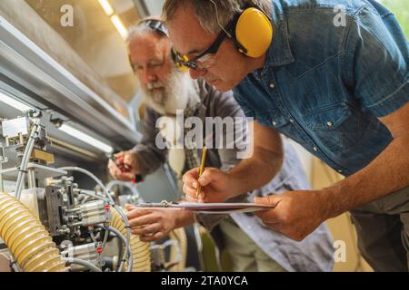 Two men with ear defenders working on machinery in a woodworking shop Stock Photo