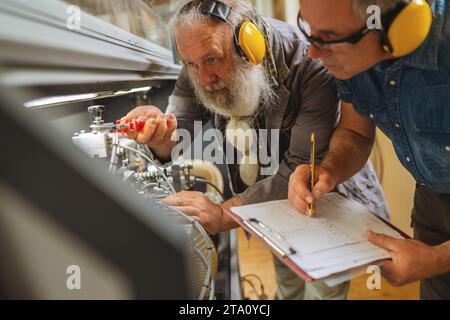 Men with ear protection adjusting machinery in a carpentry workshop Stock Photo