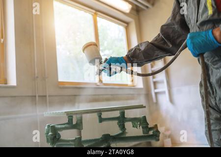 Person in protective gear using a spray gun to paint a wooden panel in a carpentry workshop Stock Photo