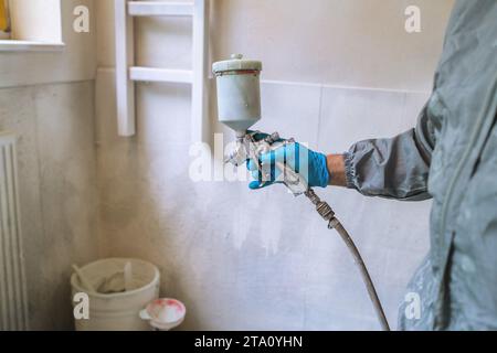 Worker using a spray gun to paint, wearing safety gloves and protective clothing Stock Photo