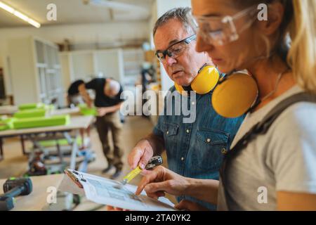 Two carpenters reviewing a blueprint with another working in the background Stock Photo