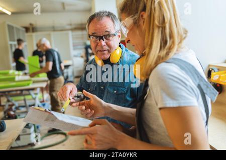 Instructor explaining measurements on blueprint to apprentice in a carpentry workshop Stock Photo