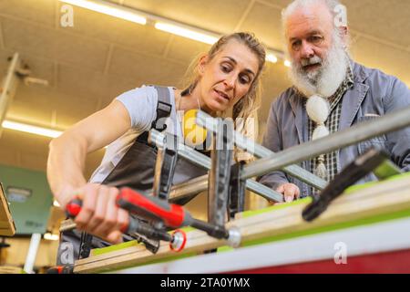 Master carpenter and apprentice using a clamp for wood gluing in a workshop Stock Photo