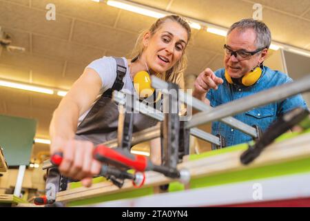Apprentice and instructor working with clamps and wood in a bright workshop Stock Photo