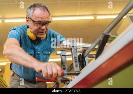 Focused Carpenter with hearing protection working with clamps and wood in a workshop Stock Photo