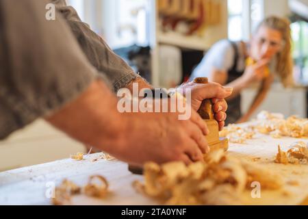 Apprentice observing with interest as a carpenter planes wood in a workshop Stock Photo