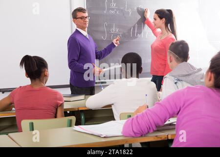 Cute schoolgirl solves task near blackboard in classroom mathematics Stock Photo