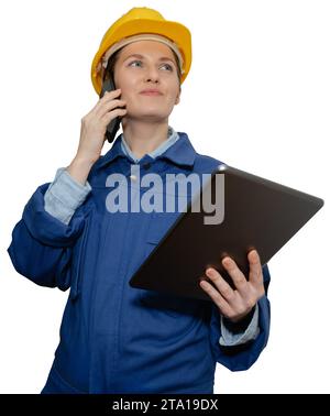 Isolated smiling woman engineer in yellow helmet and blue uniform with phone and digital tablet. Stock Photo
