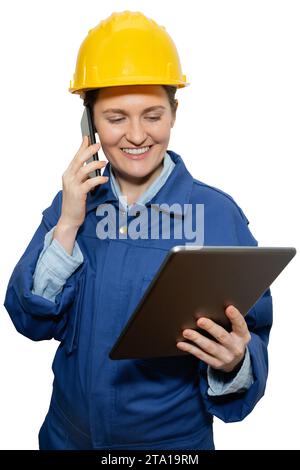 Isolated smiling woman engineer in yellow helmet and blue uniform with phone and digital tablet. Stock Photo