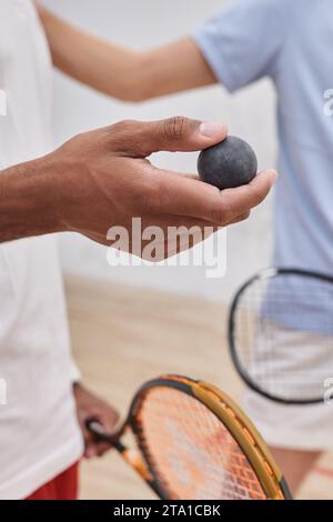 cropped shot of african american man holding squash ball near friend inside of court, vertical Stock Photo