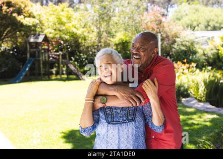 Happy diverse senior couple embracing in sunny garden. Lifestyle, retirement, senior lifestyle, nature, togetherness and domestic life, unaltered. Stock Photo