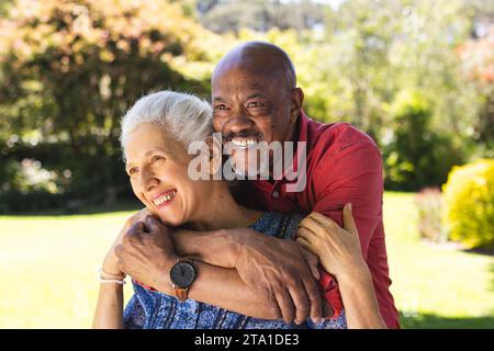 Happy diverse senior couple embracing in sunny garden. Lifestyle, retirement, senior lifestyle, nature, togetherness and domestic life, unaltered. Stock Photo