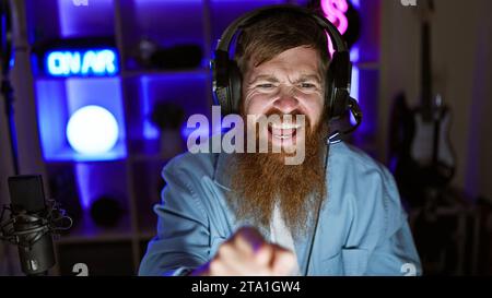 Cheerful young redhead streamer celebrates epic win. man playing video game, pointing at camera in home gaming room Stock Photo