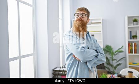 Serious-looking young irish redhead business man, elegantly dressed, purposefully standing with arms crossed at the office, concentrating on success. Stock Photo