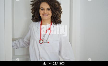 Young beautiful hispanic woman doctor smiling confident coming through the door at clinic Stock Photo