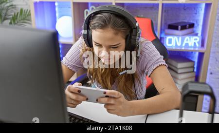 Attractive young hispanic female gamer, rocking the gaming night in her home office - an adrenaline-fueled stream as she smiles, playing smartphone vi Stock Photo