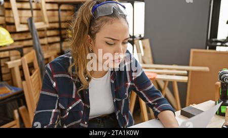 Passionate hispanic carpenter, portrait of a young, beautiful woman with serious face, professional equipment, amidst sawdust in her carpentry worksho Stock Photo