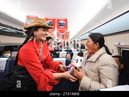 (231128) -- MAOXIAN, Nov. 28, 2023 (Xinhua) -- A performer presents a souvenir to a passenger on the first high-speed passenger train C6008 on a section of the Sichuan-Qinghai railway, Nov. 28, 2023. A 238-km section of the Sichuan-Qinghai railway in western China became operational on Tuesday after 12 years of construction.   The railway crosses the rugged, earthquake-prone plateau region in northwest Sichuan, and takes a detour to avoid disturbing the Giant Panda National Park.      The Sichuan-Qinghai railway will eventually stretch northwestward to Xining, the capital city of Qinghai Provi Stock Photo