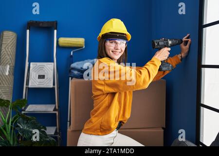 Young blonde woman wearing hardhat using dirll on wall at new home Stock Photo