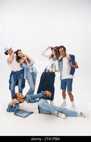 happy african american man lying down and looking at trendy interracial friends embracing on grey Stock Photo
