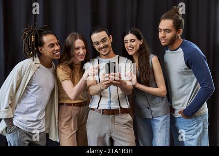 cheerful manager using smartphone near multicultural team on black backdrop in office, group photo Stock Photo
