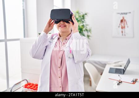 Young beautiful plus size woman doctor using virtual reality glasses at clinic Stock Photo