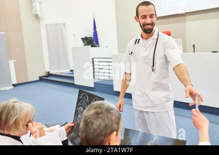 Smiling male orator giving pens to doctors with x-rays during medical conference at auditorium Stock Photo