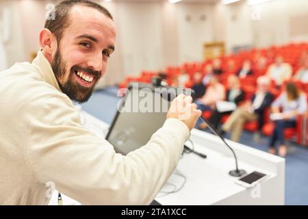 Portrait of smiling speaker giving speech through microphone at podium in seminar at convention center Stock Photo