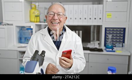 Senior man scientist smiling confident using smartphone at laboratory Stock Photo