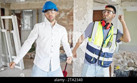 Two men builder and architect smiling confident dancing at construction site Stock Photo