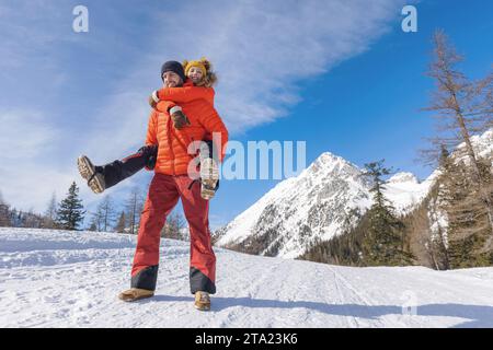 Man carries his girlfriend on his back in snowy mountain area Stock Photo