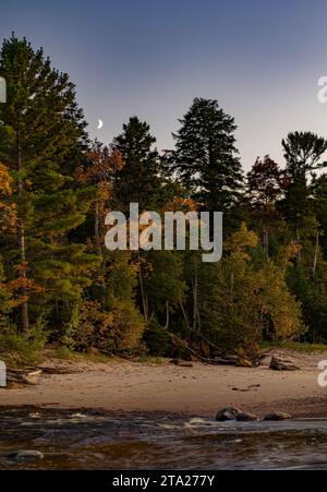 The moon rises over the forest at the Lake Superior shore at Hurricane River beach in Pictured Rocks National Lakeshore, Alger County, Michigan Stock Photo