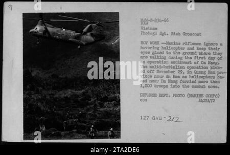 Marine riflemen maintain focus on the ground as a helicopter hovers nearby during the start of a military operation south-west of Da Nang in Vietnam. The operation, which began on November 29, 1966, involved multiple battalions and saw over 1,000 troops transported by helicopters from Da Nang into the combat zone. Stock Photo