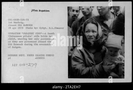 A South Vietnamese woman, the wife of a pilot, carries her child and their few belongings as they are processed aboard the USS Hancock during the evacuation of Saigon on April 29, 1975, as part of Operation Frequent Wind. This photograph was taken by GySgt. D.L. Shearer and released by the Defense Department. (127 GVB-279) Stock Photo