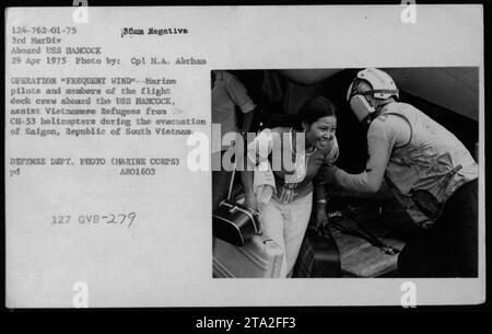 Marine pilots and flight deck crewmembers are seen assisting Vietnamese refugees from CH-53 helicopters aboard the USS HANCOCK during the evacuation of Saigon on April 29, 1975. This image captures a moment from Operation Frequent Wind, which aimed to evacuate Americans and Vietnamese citizens during the chaos of the Vietnam War. Stock Photo