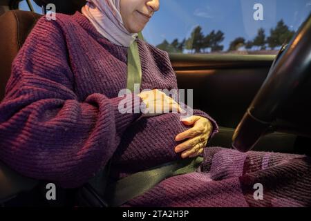 Pregnant arabic muslim woman driving car at night wearing winter clothes ,hijab and seat belt driving in confidently and feeling safe Stock Photo