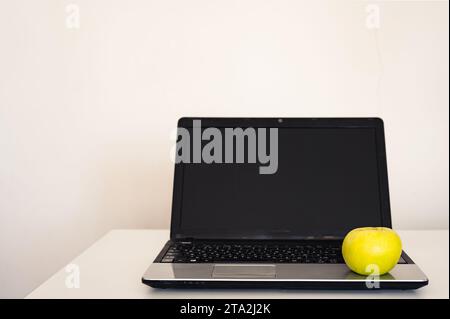 Empty open laptop with mockup and black screen on white desk table. Yellow apple. Minimalist workspace Stock Photo