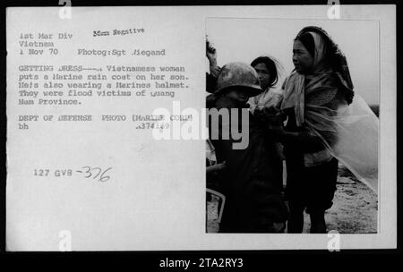 Vietnamese woman helps her son put on a large raincoat and a Marine Corps helmet as they recover from the floods in Quang Nam Province. This photograph from November 1, 1970 captures a moment of civilian life during the Vietnam War. Department of Defense photo (Marine Corps), Sgt. Liegand is the photographer. Stock Photo