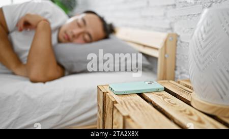 Exhausted young chinese man comfortably lying in bed, falling asleep in his cozy bedroom after relaxing morning with his phone Stock Photo