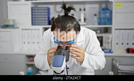 Focused young chinese man, a dedicated scientist at the heart of medical technology, deeply immersed in biology research using microscope in lab. Stock Photo
