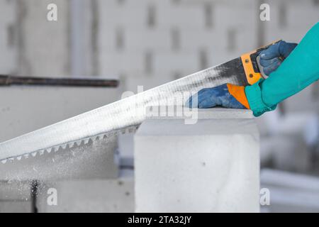 A worker at a construction site saws a building block from aerated concrete at a construction site Stock Photo