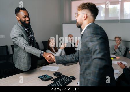 Back view handshaking of happy African-American and Caucasian businessmen partner after signing contract at group negotiations getting team applause Stock Photo