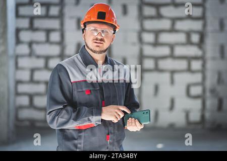 Caucasian construction worker in overalls and helmet uses a smartphone with cameras in his professional work Stock Photo