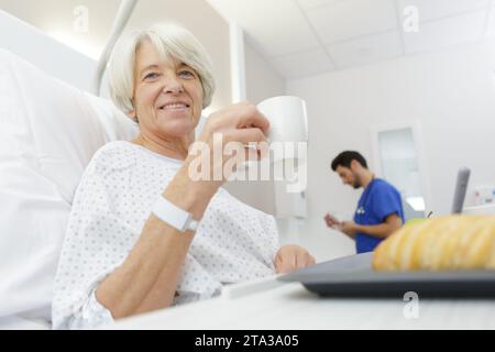 senior female patient holding mug and drinking coffee on bed Stock Photo