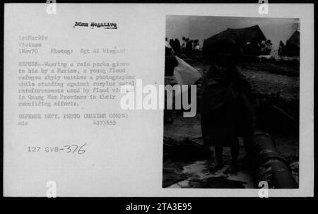 Vietnamese civilian, a flood refugee in Quang Nam province, wearing a rain parka given by a Marine, stands against metal reinforcements used in rebuilding efforts. Photograph taken on November 1, 1970, by Sgt. Al Wiegand, during the Vietnam War, by the US Department of Defense (Marine Corps). Image ID: A373655 127 GVB-376. Stock Photo